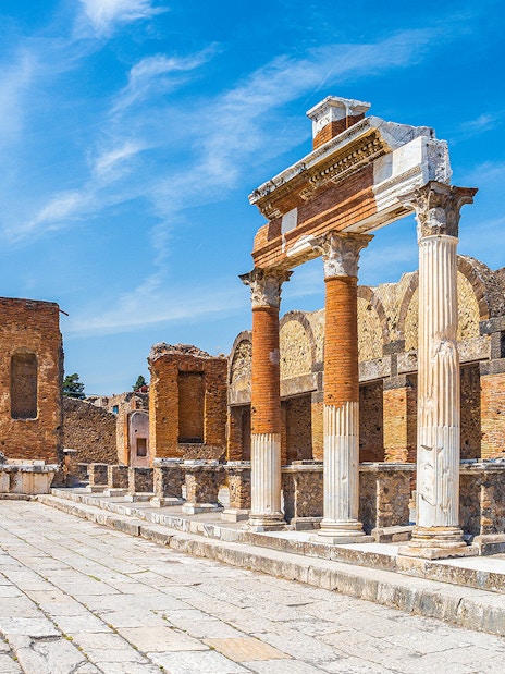 Ancient ruins of Pompeii with stone columns and archway under a clear blue sky.
