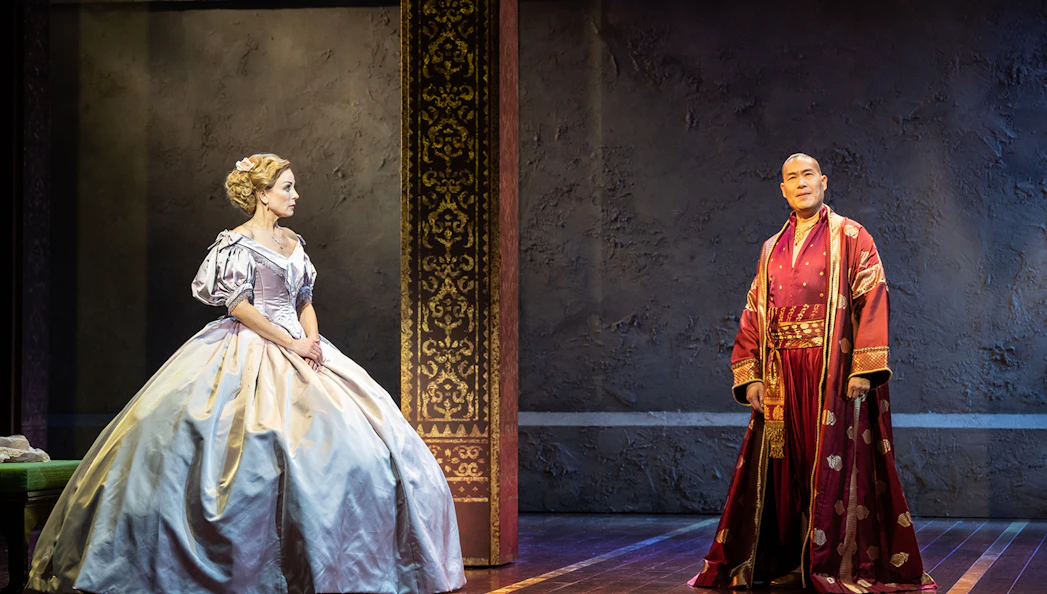 Stage scene from "The King and I" with two actors in period costumes.