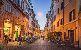 Evening street scene in Rome with people walking and scooters parked, part of Ghosts of Rome tour.