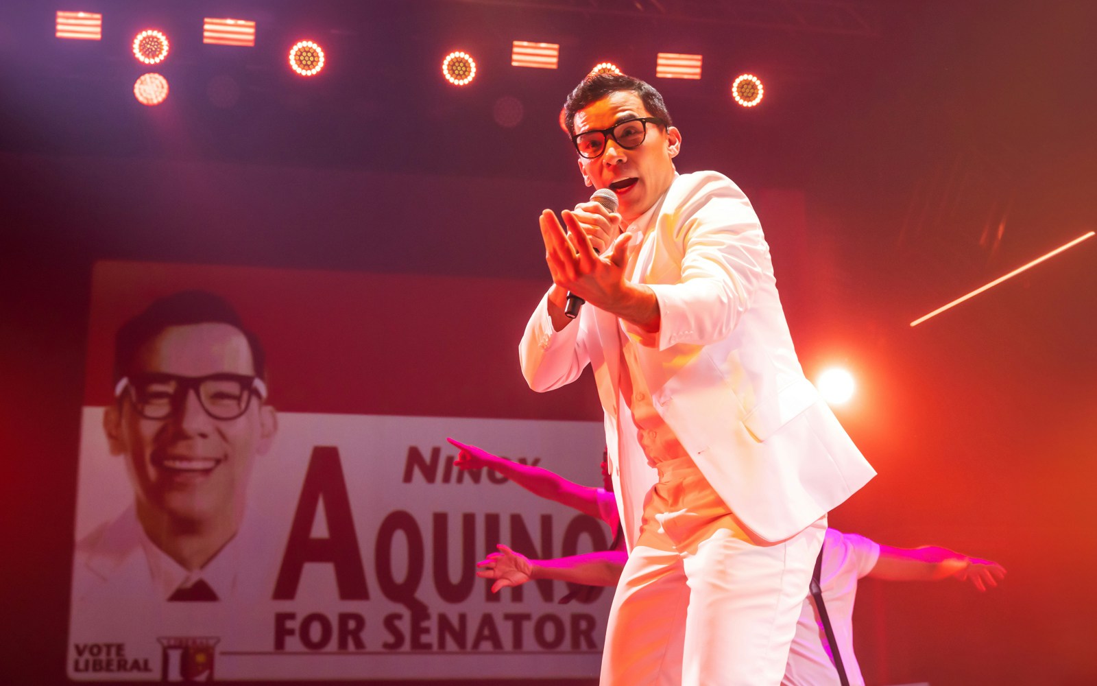 Performer on stage during "Here Lies Love" musical with campaign poster backdrop.