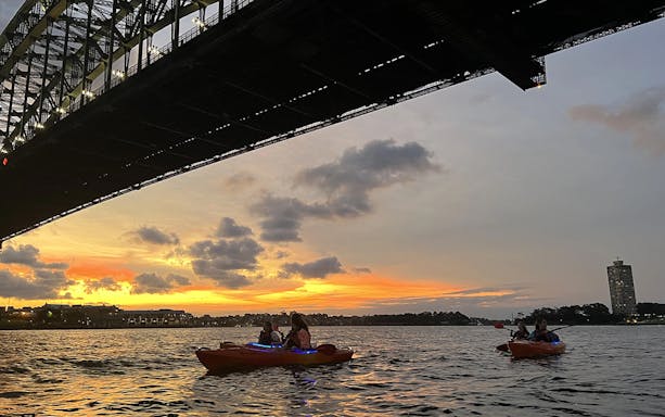 Kayakers paddle under Sydney Harbour Bridge at sunset on Sydney Harbour.