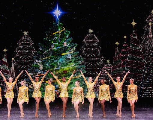 Radio City Rockettes performing in front of a decorated Christmas tree.