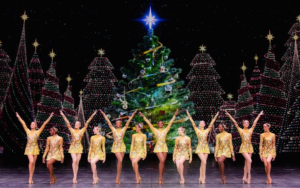 Radio City Rockettes performing in front of a decorated Christmas tree.