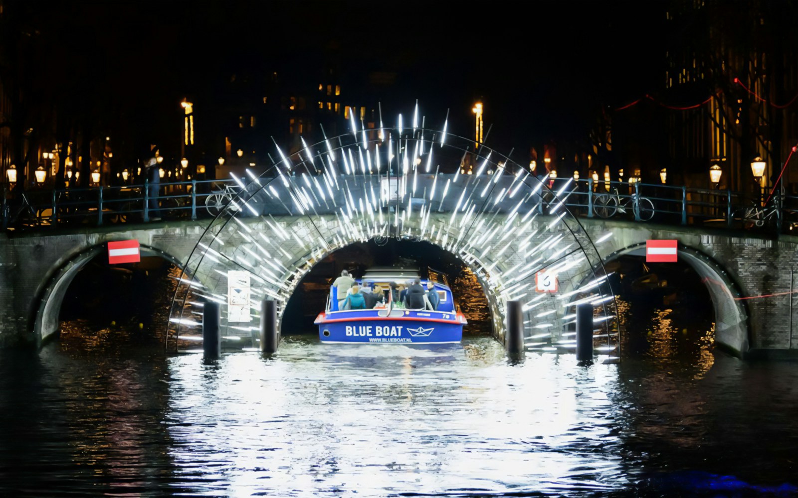 Boat passing under illuminated bridge at Amsterdam Light Festival.