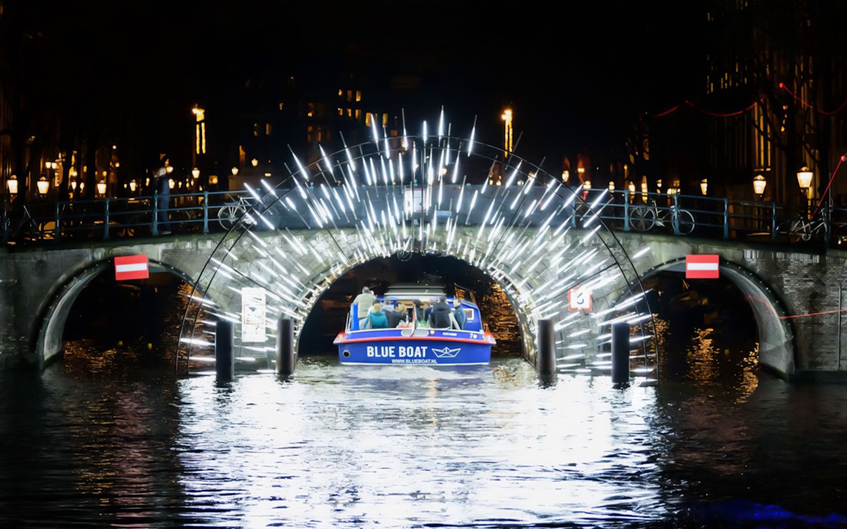 Boat passing under illuminated bridge at Amsterdam Light Festival.