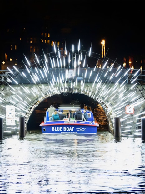 Boat passing under illuminated bridge at Amsterdam Light Festival.
