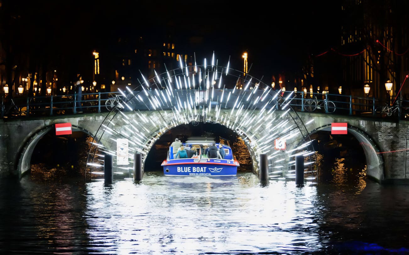 Boat passing under illuminated bridge at Amsterdam Light Festival.
