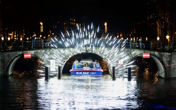 Boat passing under illuminated bridge at Amsterdam Light Festival.