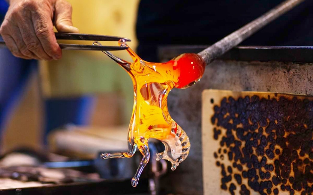 Glass artisan shaping molten glass in Murano workshop.