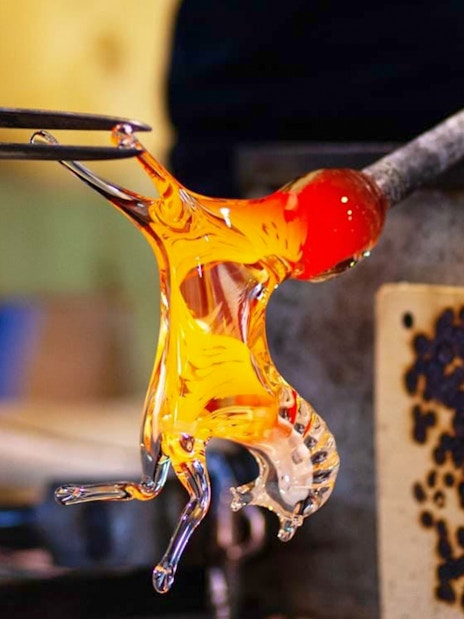 Glass artisan shaping molten glass in Murano workshop.