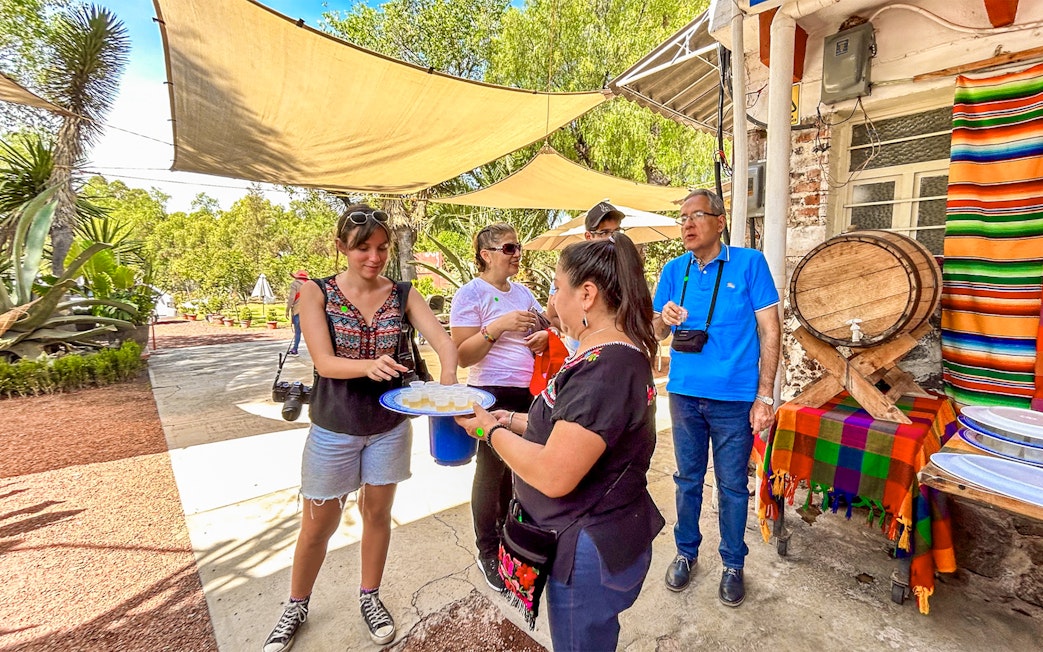 Tourists sampling tequila outdoors near a colorful table and barrel in Mexico.