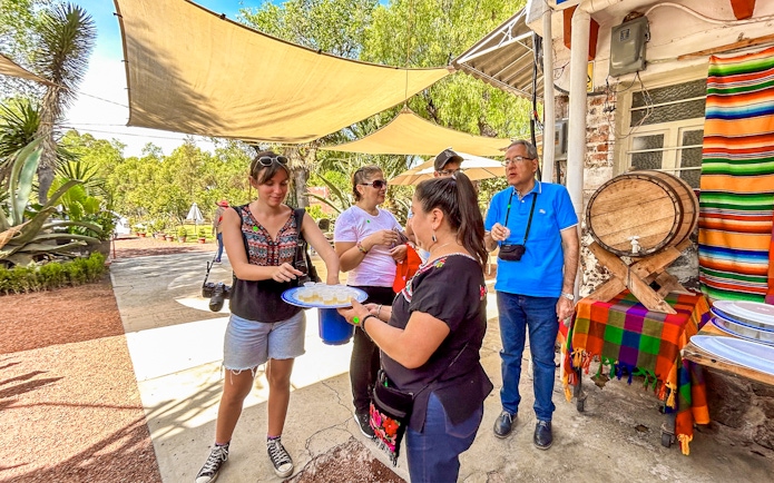 Tourists sampling tequila outdoors near a colorful table and barrel in Mexico.
