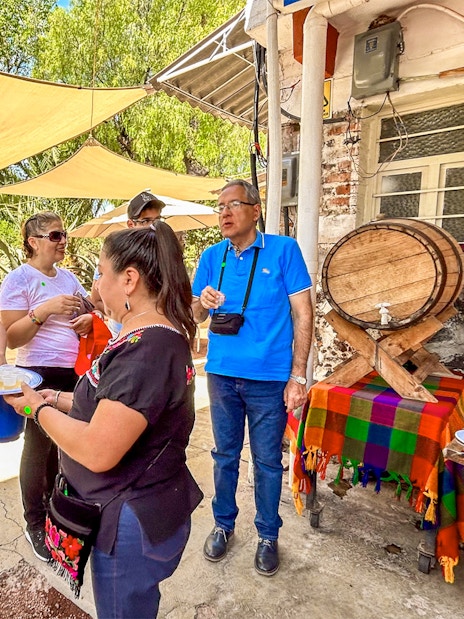 Tourists sampling tequila outdoors near a colorful table and barrel in Mexico.