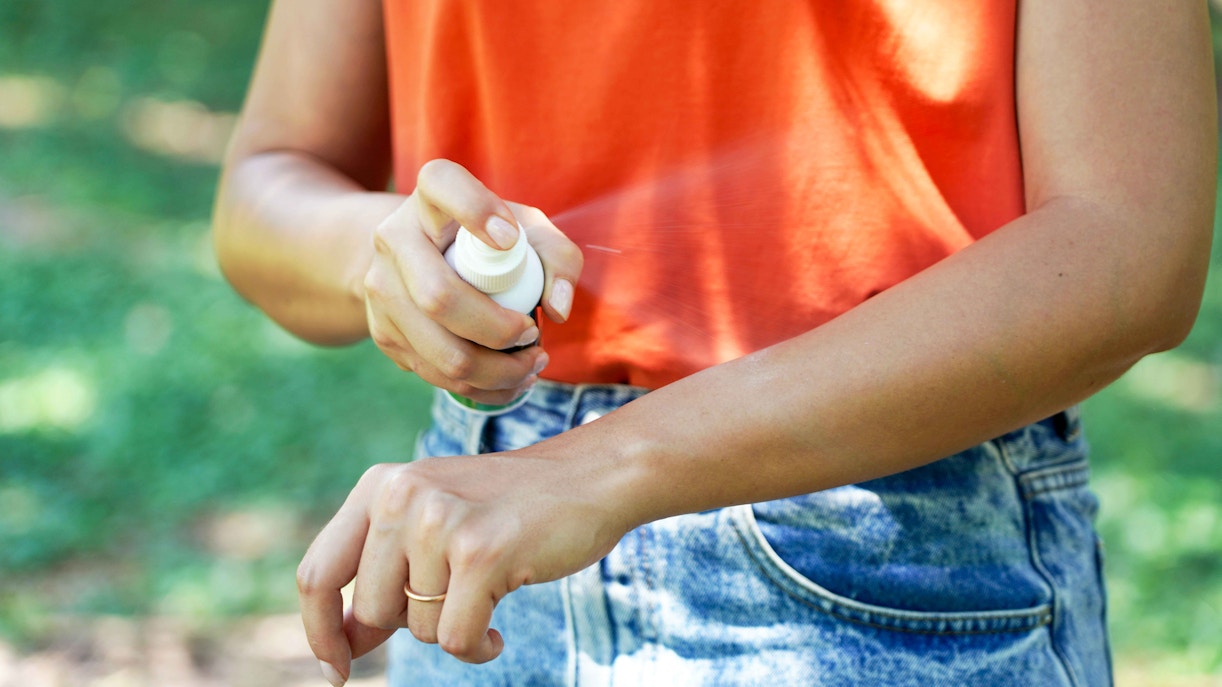 Girl applying insect repellent on arm in tropical outdoor setting.