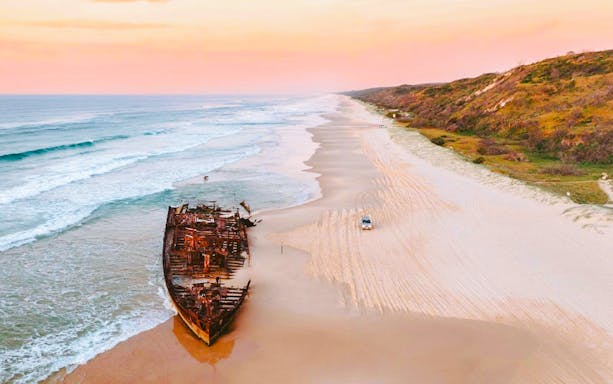 SS Maheno shipwreck on 75 Mile Beach, Fraser Island, with a car driving along the shore.
