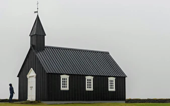 Black church at Búðir on Snaefellsnes Peninsula, Iceland, with a person standing nearby.