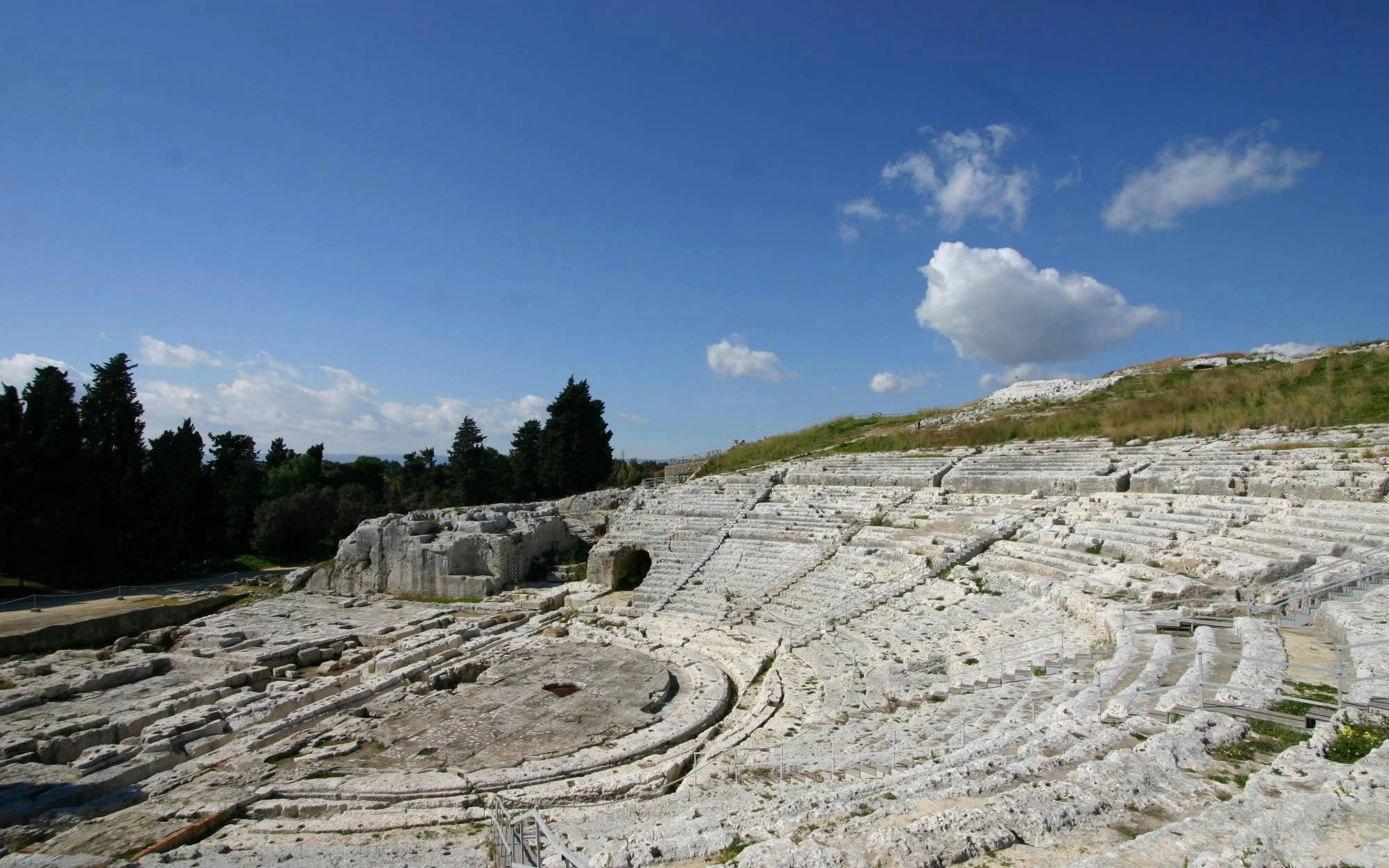 Greek Theater ruins in Neapolis, Syracuse, with stone seating and open sky.