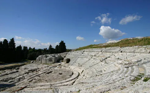 Greek Theater ruins in Neapolis, Syracuse, with stone seating and open sky.