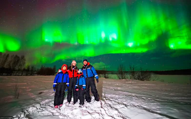 Guests on Northern Lights tour under vibrant aurora in snowy landscape.