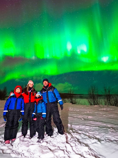 Guests on Northern Lights tour under vibrant aurora in snowy landscape.