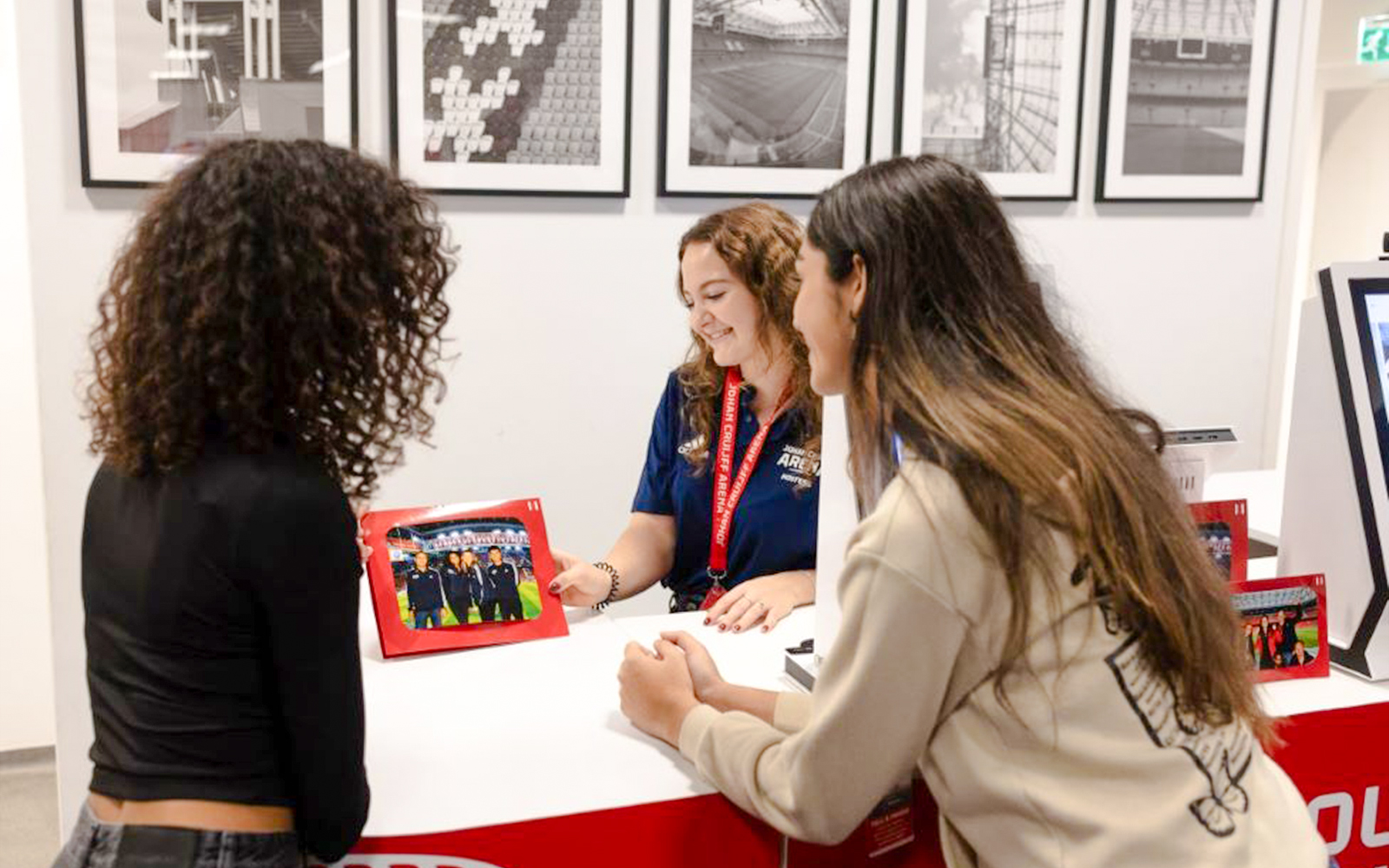 Visitors at Johan Cruijff ArenA tour desk with stadium photos in background.