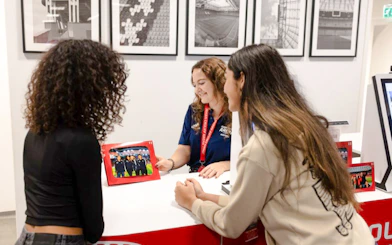 Visitors at Johan Cruijff ArenA tour desk with stadium photos in background.