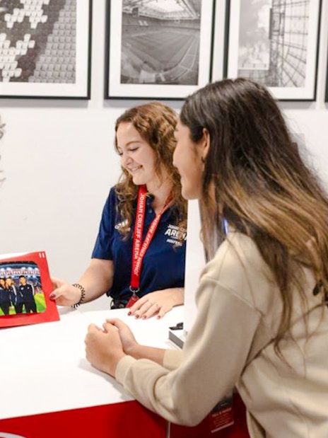 Visitors at Johan Cruijff ArenA tour desk with stadium photos in background.