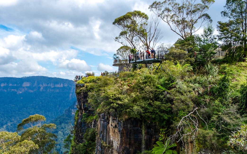 Visitors on a lookout platform at Blue Mountains viewpoint, surrounded by lush greenery.