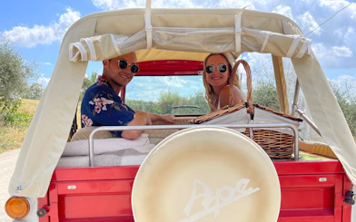 Couple enjoying a Tuscany tuk tuk tour with picnic basket on a sunny day.