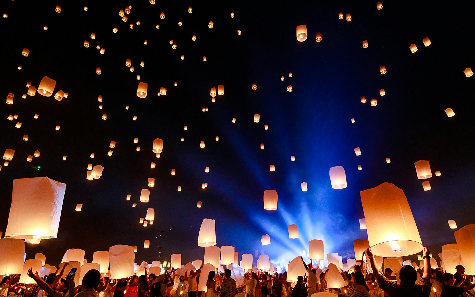 People releasing lanterns into the night sky at Chiang Mai Sky Lanterns Festival 2025.