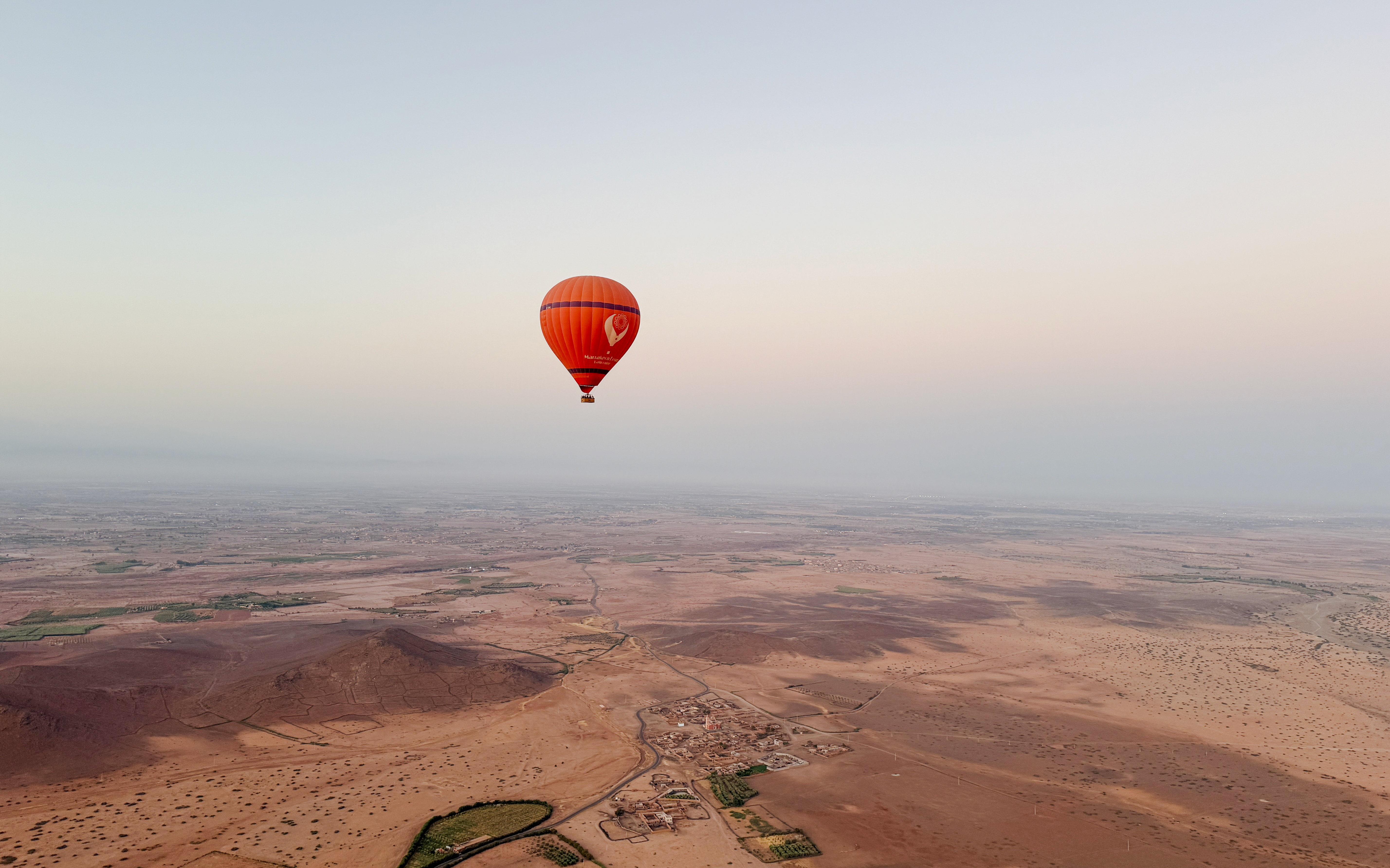 Hot air balloon over Marrakech desert landscape at sunrise.