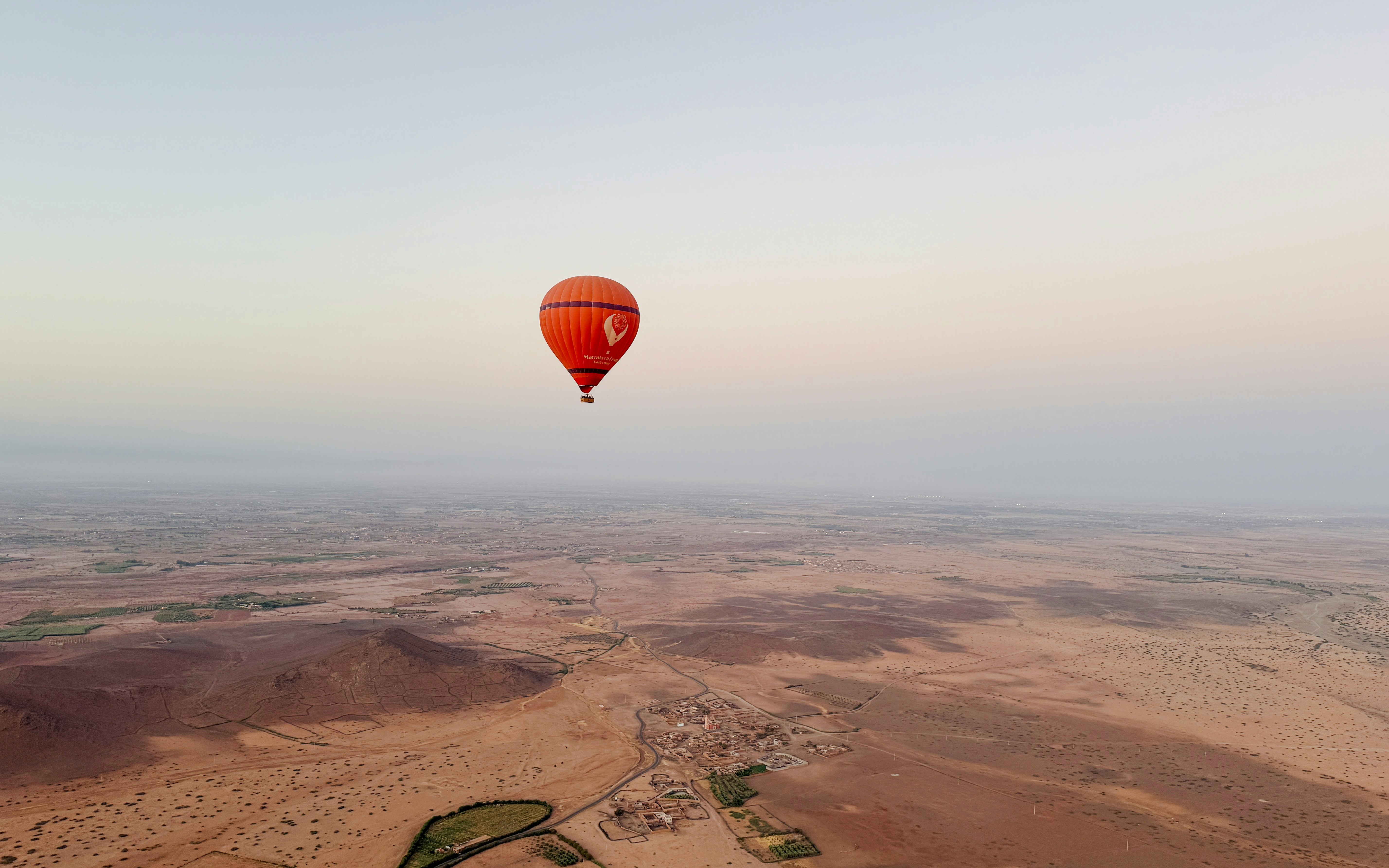 Hot air balloon over Marrakech desert landscape at sunrise.