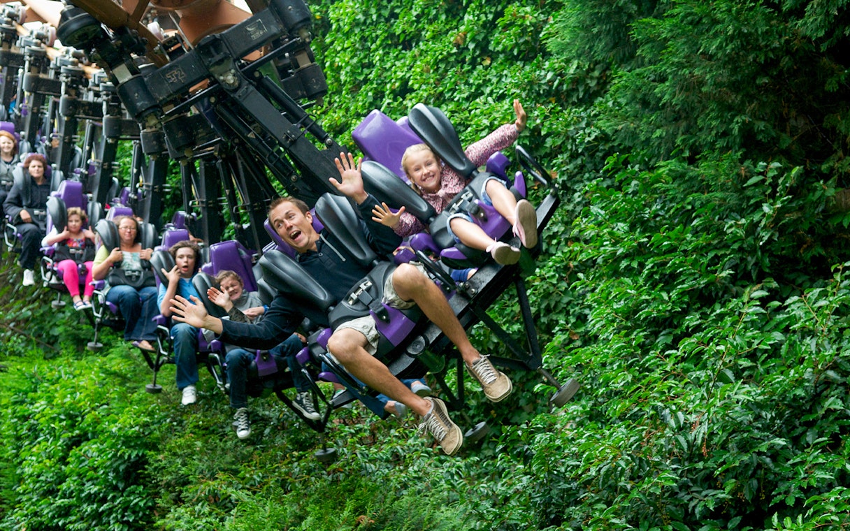 Families enjoying a thrilling rollercoaster ride through lush greenery.