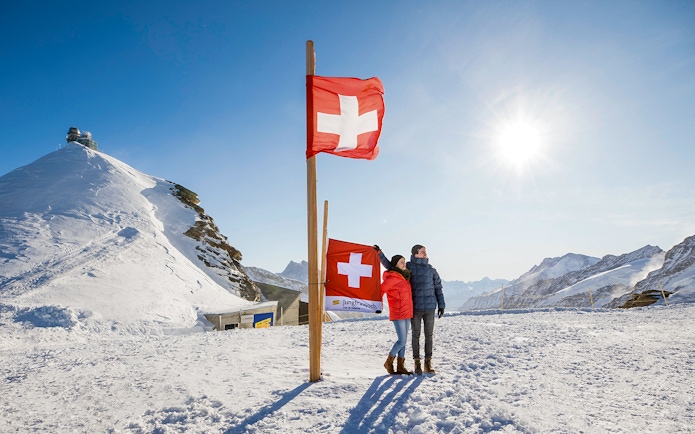 Visitors at Jungfraujoch Plateau with Swiss flags and snowy mountain backdrop.