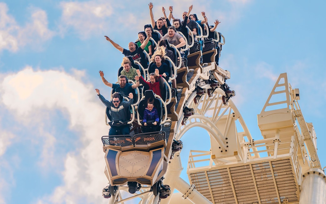 Riders with raised arms on THE SWARM roller coaster at Thorpe Park Resort, Surrey, UK.