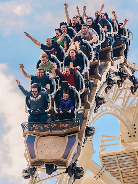 Riders with raised arms on THE SWARM roller coaster at Thorpe Park Resort, Surrey, UK.