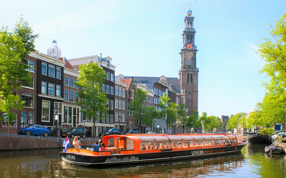 Canal cruise boat on Amsterdam canal with Westerkerk tower in the background.