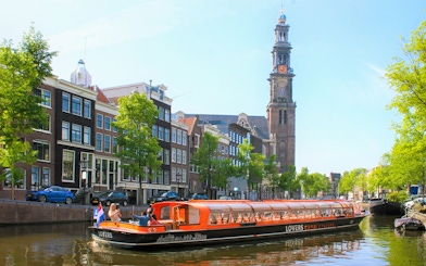 Canal cruise boat on Amsterdam canal with Westerkerk tower in the background.