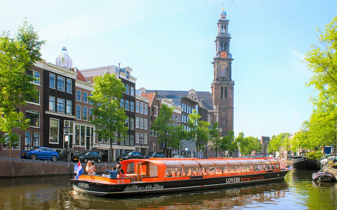Canal cruise boat on Amsterdam canal with Westerkerk tower in the background.