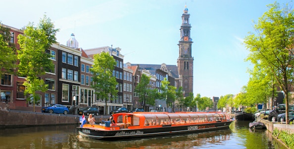 Canal cruise boat on Amsterdam canal with Westerkerk tower in the background.