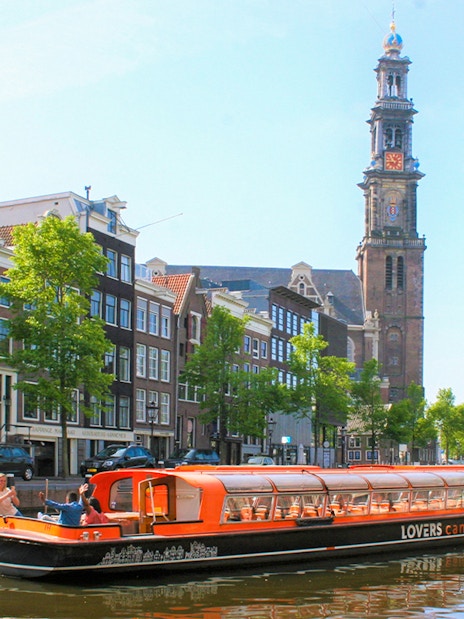 Canal cruise boat on Amsterdam canal with Westerkerk tower in the background.