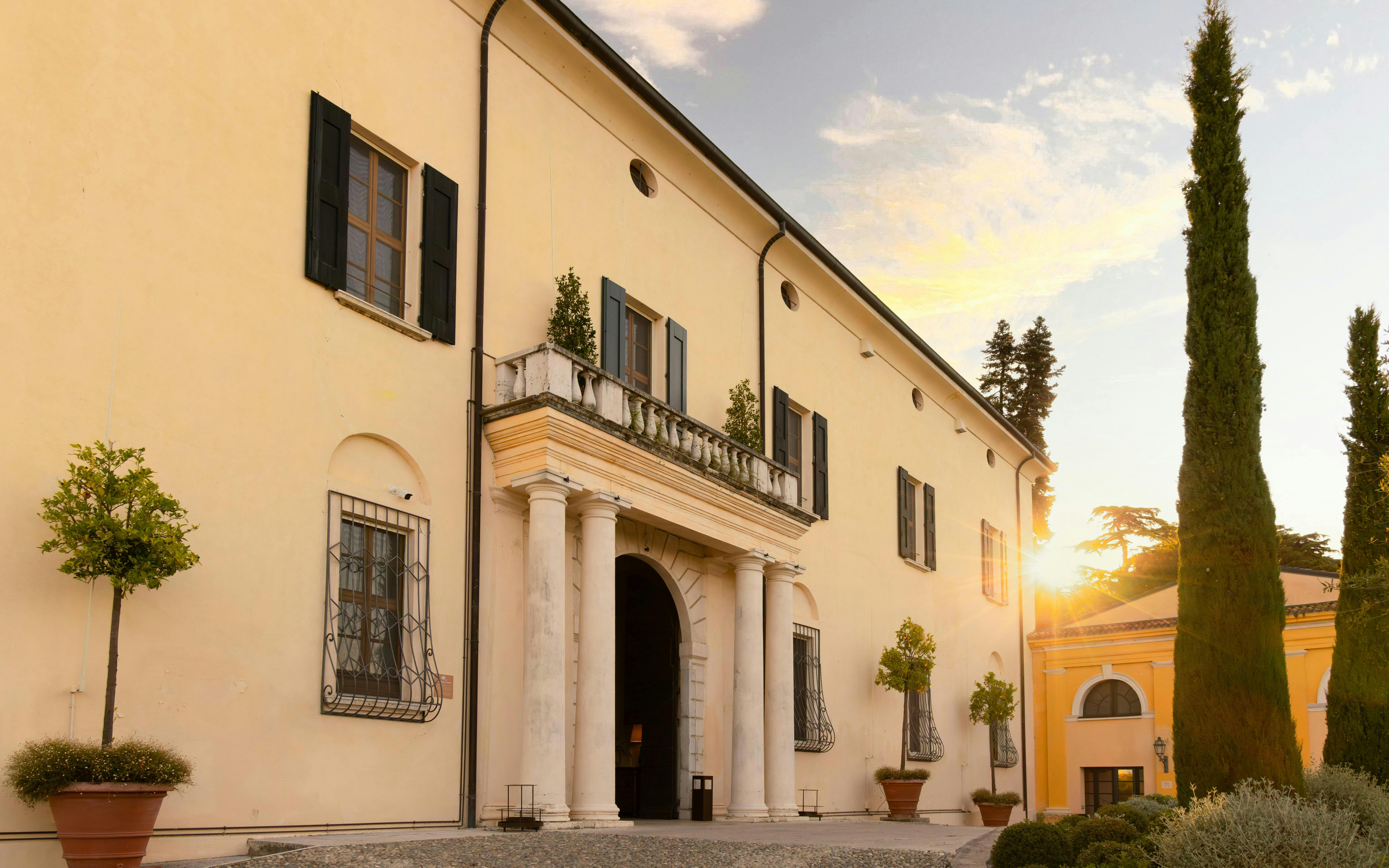 Exteriors of QC Terme Garda with sunset and cypress trees in the foreground.
