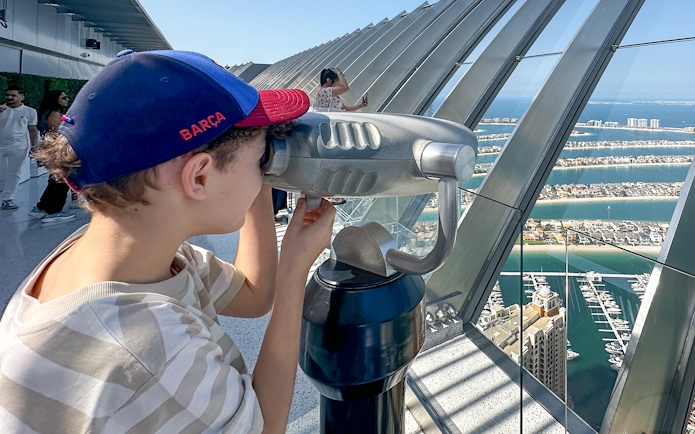 Kid using binoculars at View At The Palm, overlooking Dubai's Palm Jumeirah.