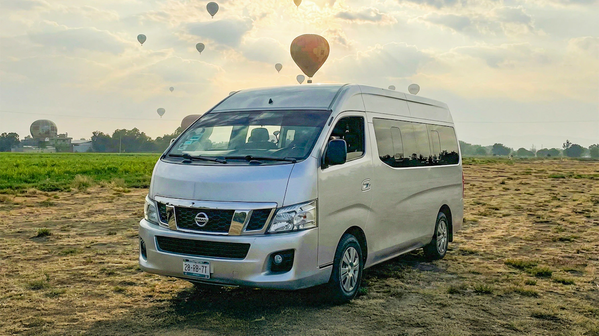 Van parked in a field with hot air balloons in the sky, Teotihuacán tour.