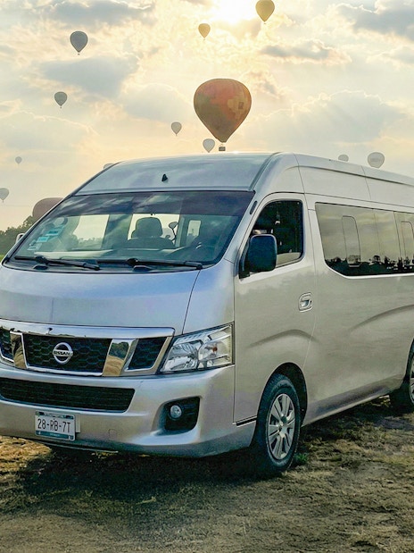 Van parked in a field with hot air balloons in the sky, Teotihuacán tour.