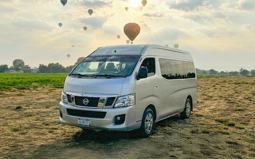 Van parked in a field with hot air balloons in the sky, Teotihuacán tour.