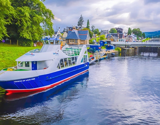 Loch Ness cruise boat docked near Inverness, Scotland, with scenic village backdrop.