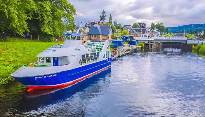 Loch Ness cruise boat docked near Inverness, Scotland, with scenic village backdrop.