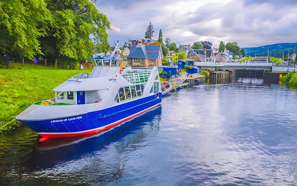 Loch Ness cruise boat docked near Inverness, Scotland, with scenic village backdrop.