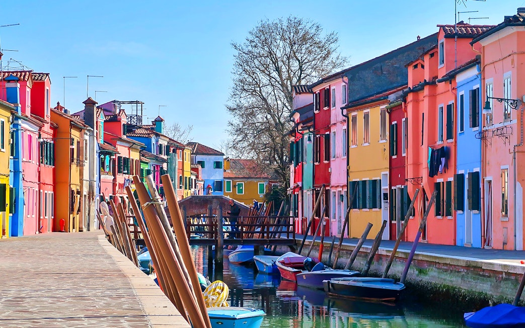 Colorful houses along a canal in Burano, Italy, with boats and a footbridge.